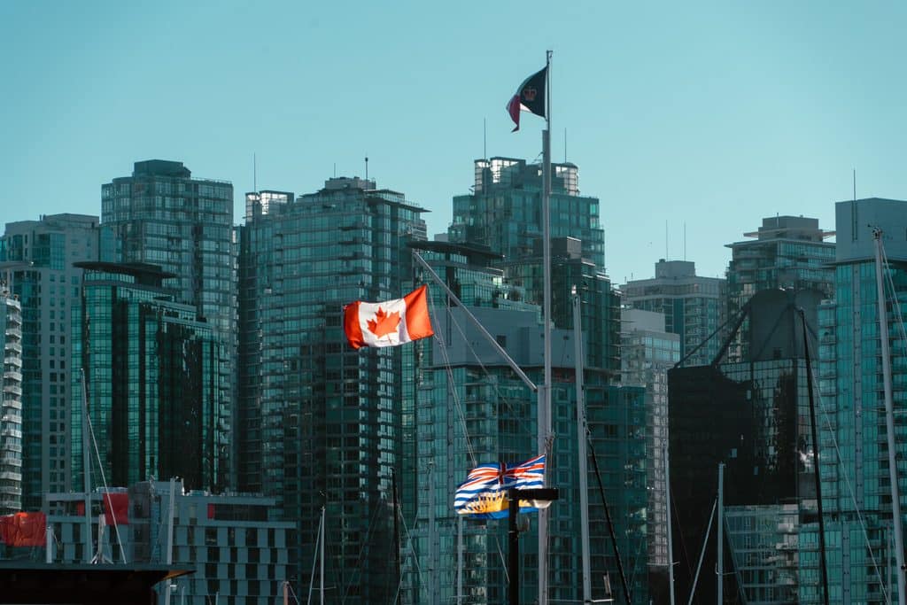 Canadian and British Columbia flags beside a marina and city buildings.